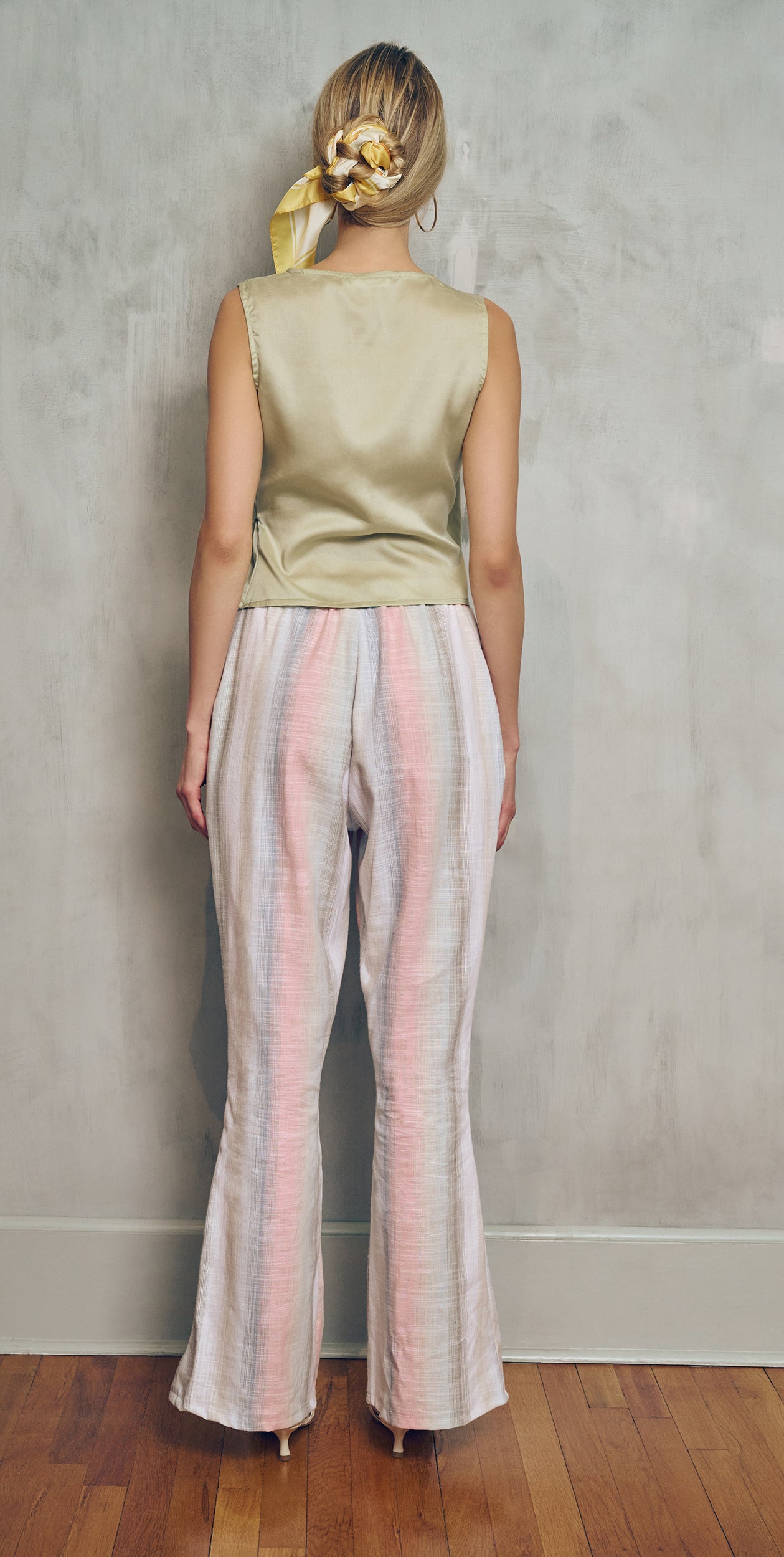 Woman wearing a sleeveless top and striped pants against a plain wall.