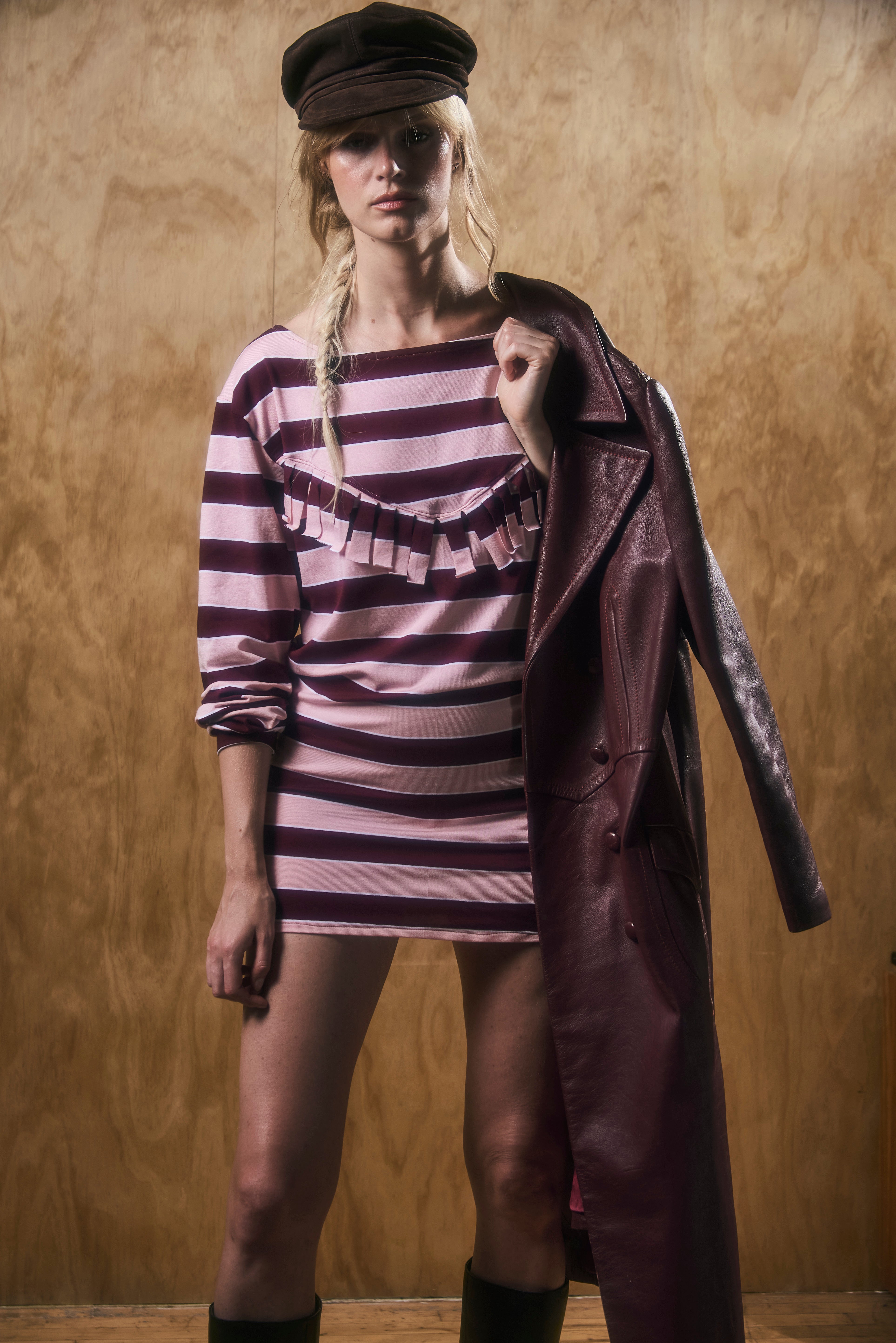 Woman wearing a striped dress and long coat against a wooden background
