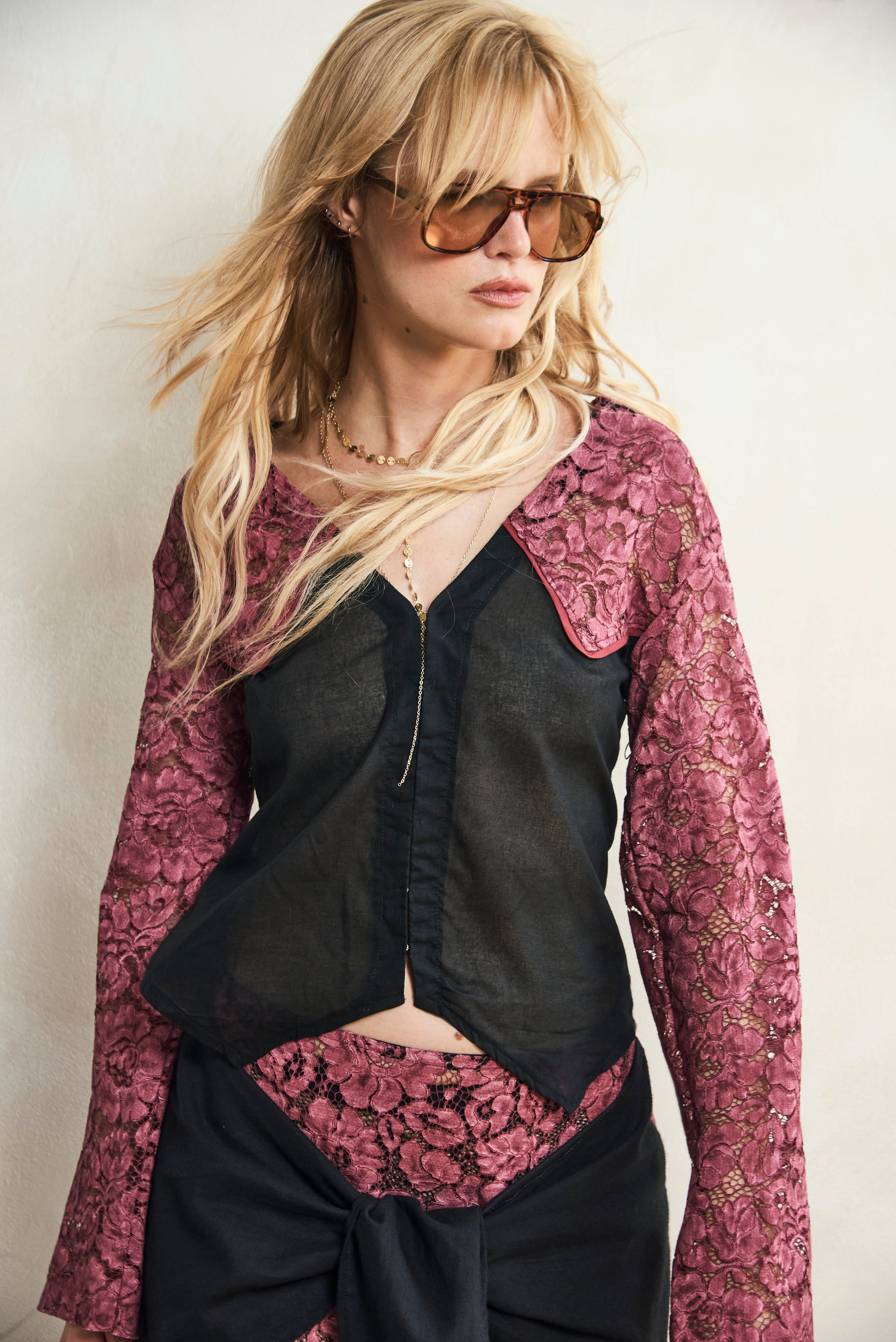 Woman wearing a black top with a pink floral lace sleeve against a white background