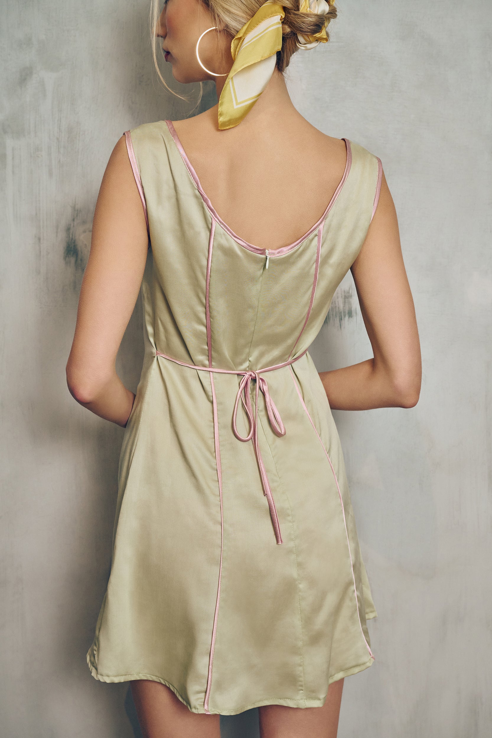 Woman wearing a light green dress with pink trim against a gray background