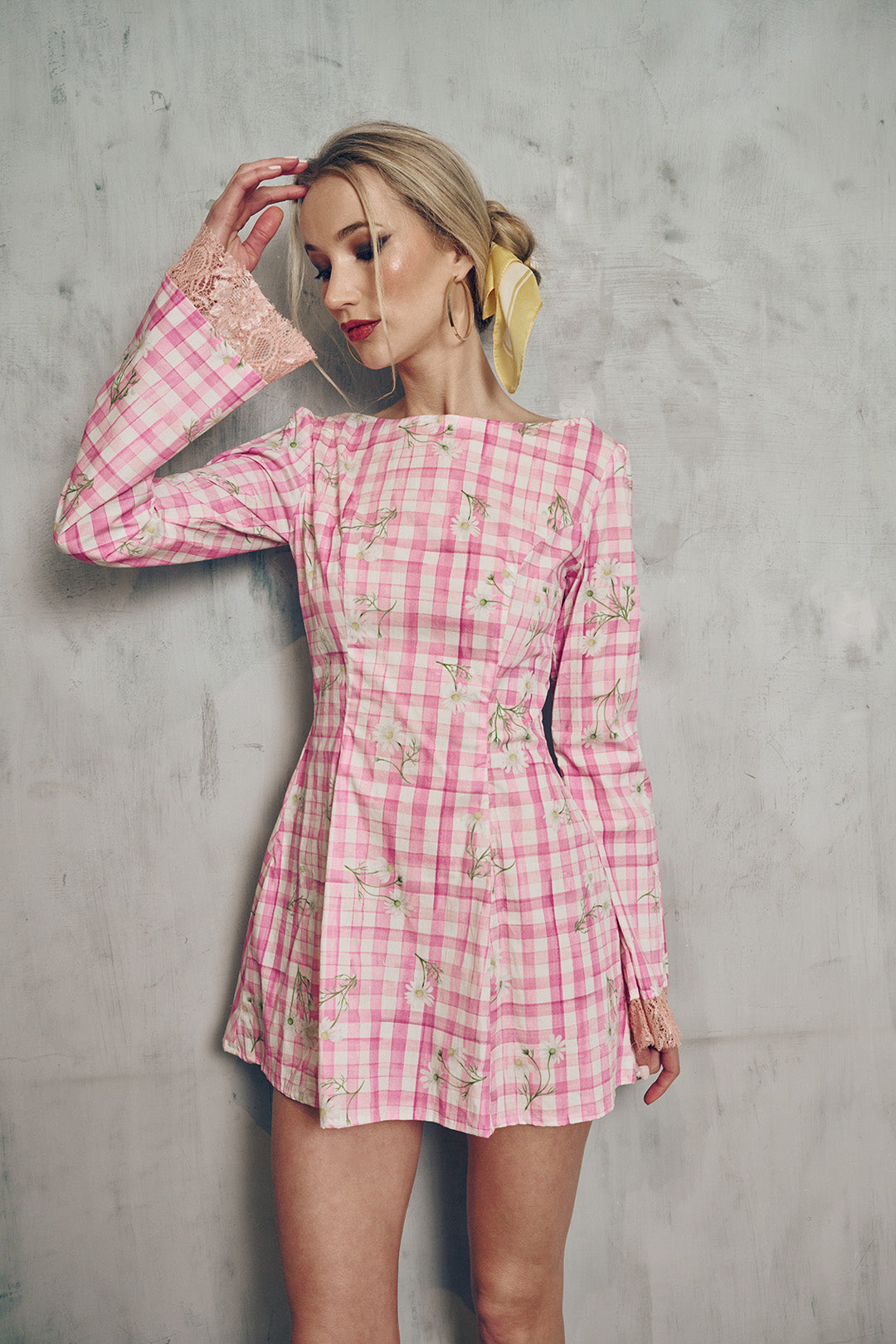 Woman wearing a pink checkered dress against a gray concrete wall