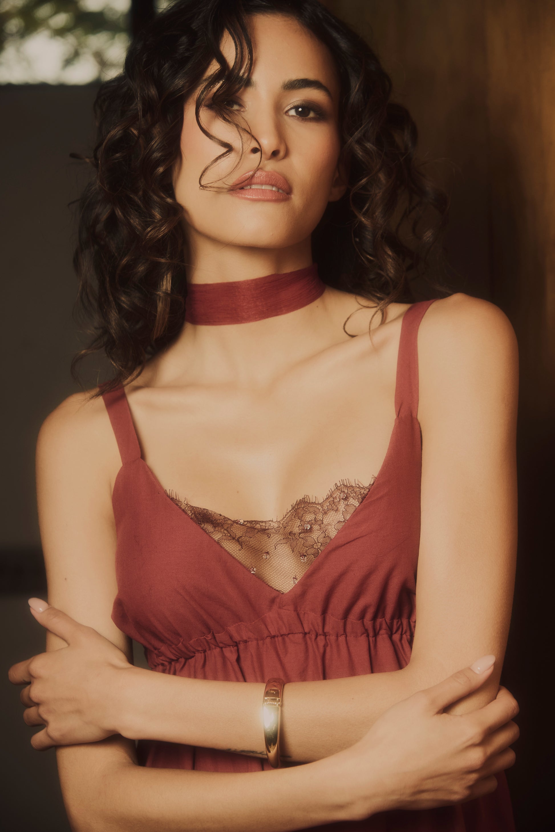 Woman wearing a red dress with a lace and beads embroidery detail in a dimly lit setting