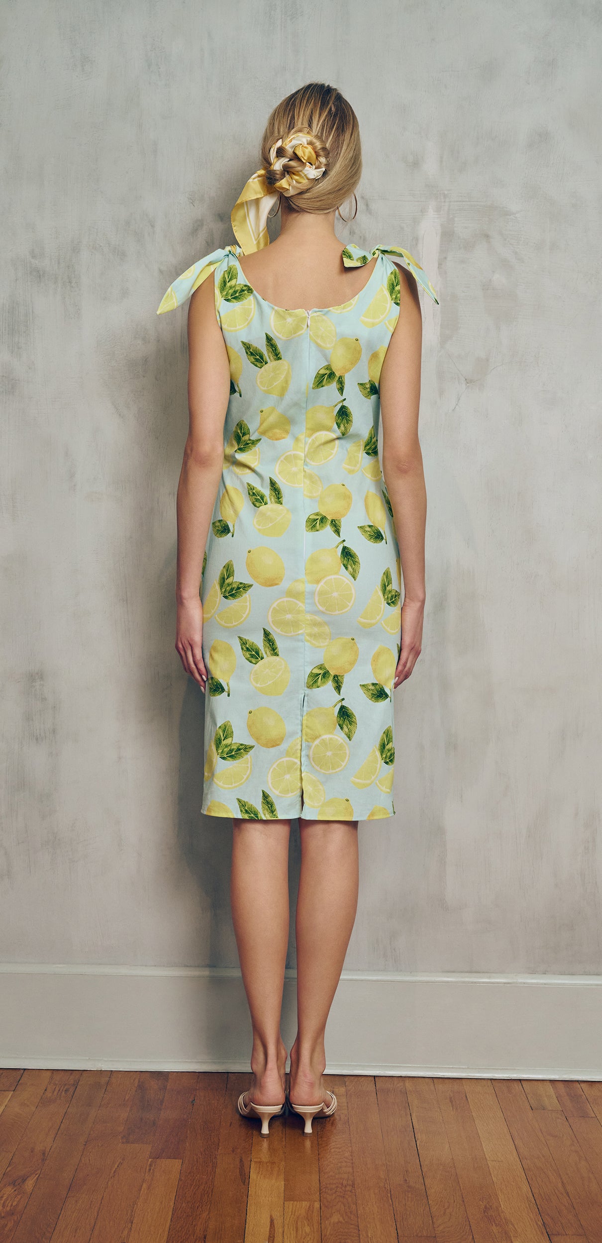 back view Woman wearing a light blue  with a lemon pattern dress against a plain background