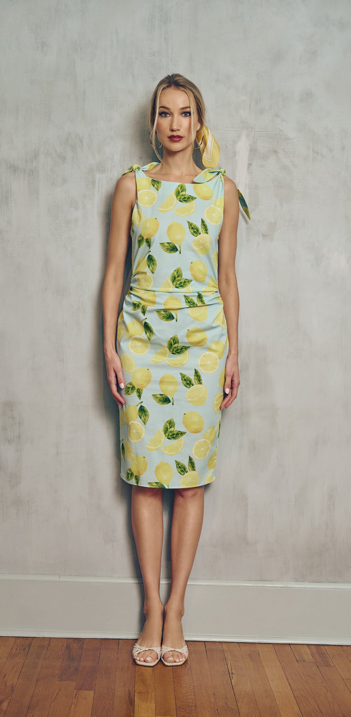 front view Woman wearing a light blue  with a lemon pattern dress against a plain background