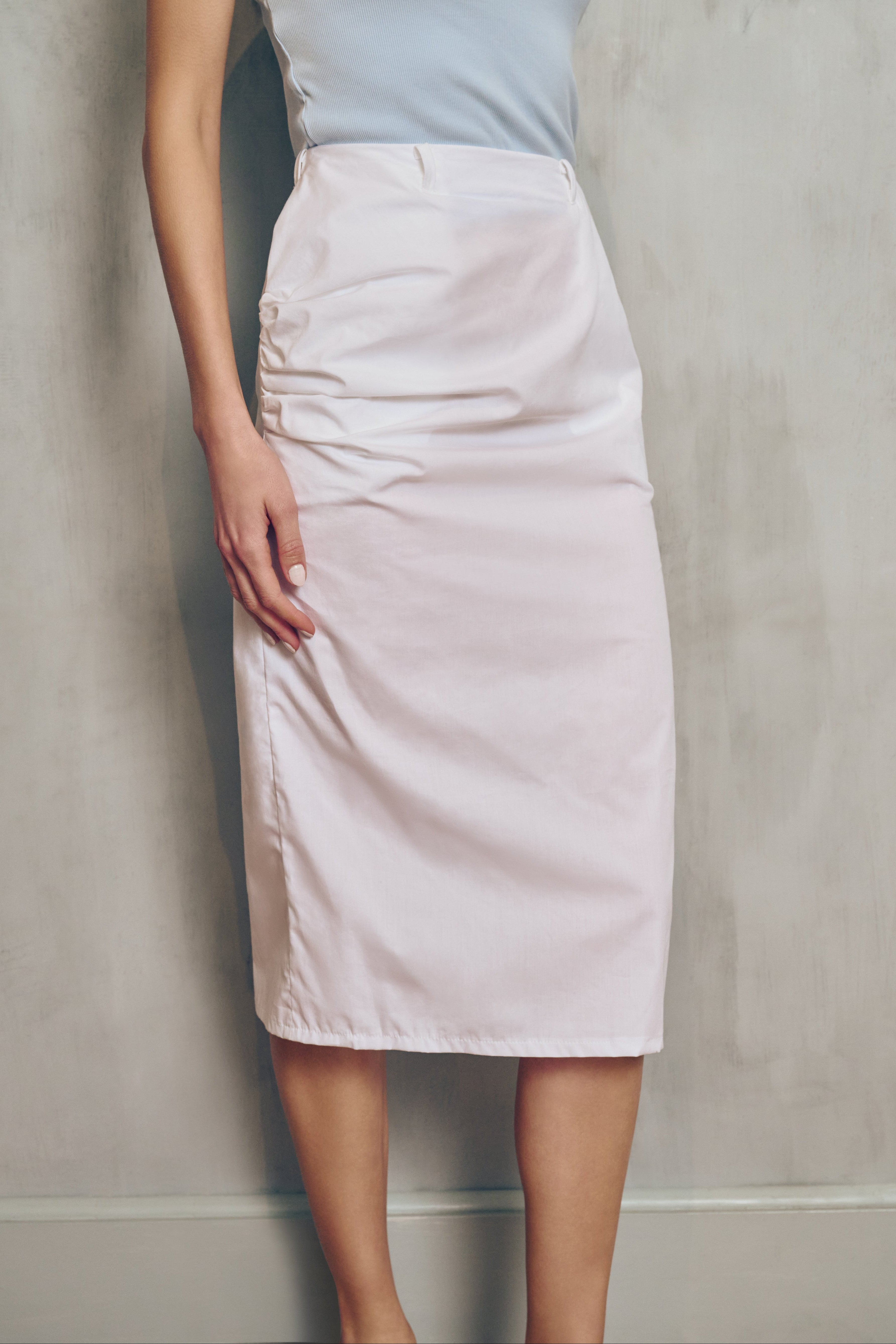 Person wearing a light blue top and white skirt against a plain background