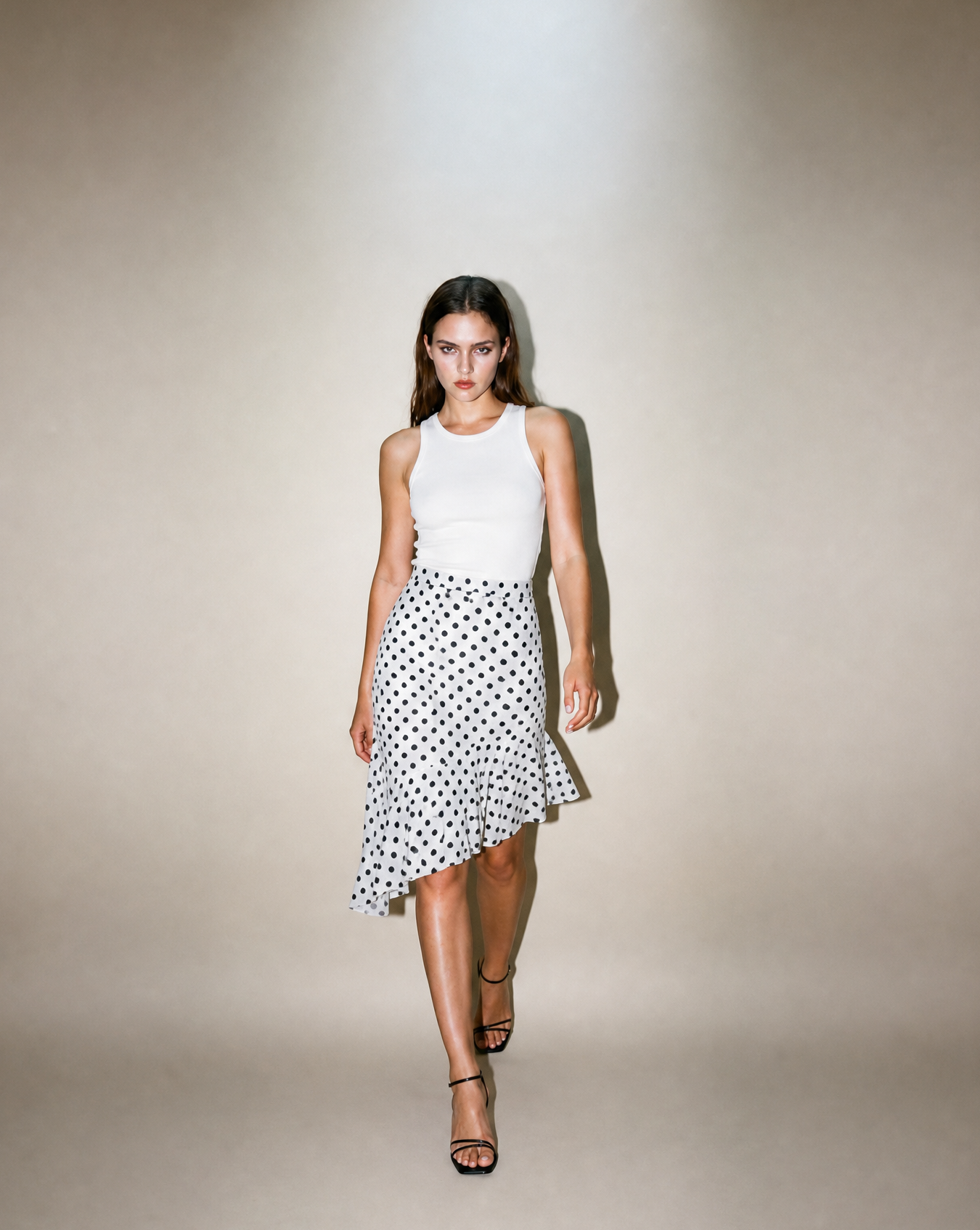 Woman wearing a white sleeveless top and polka dot skirt on a plain background