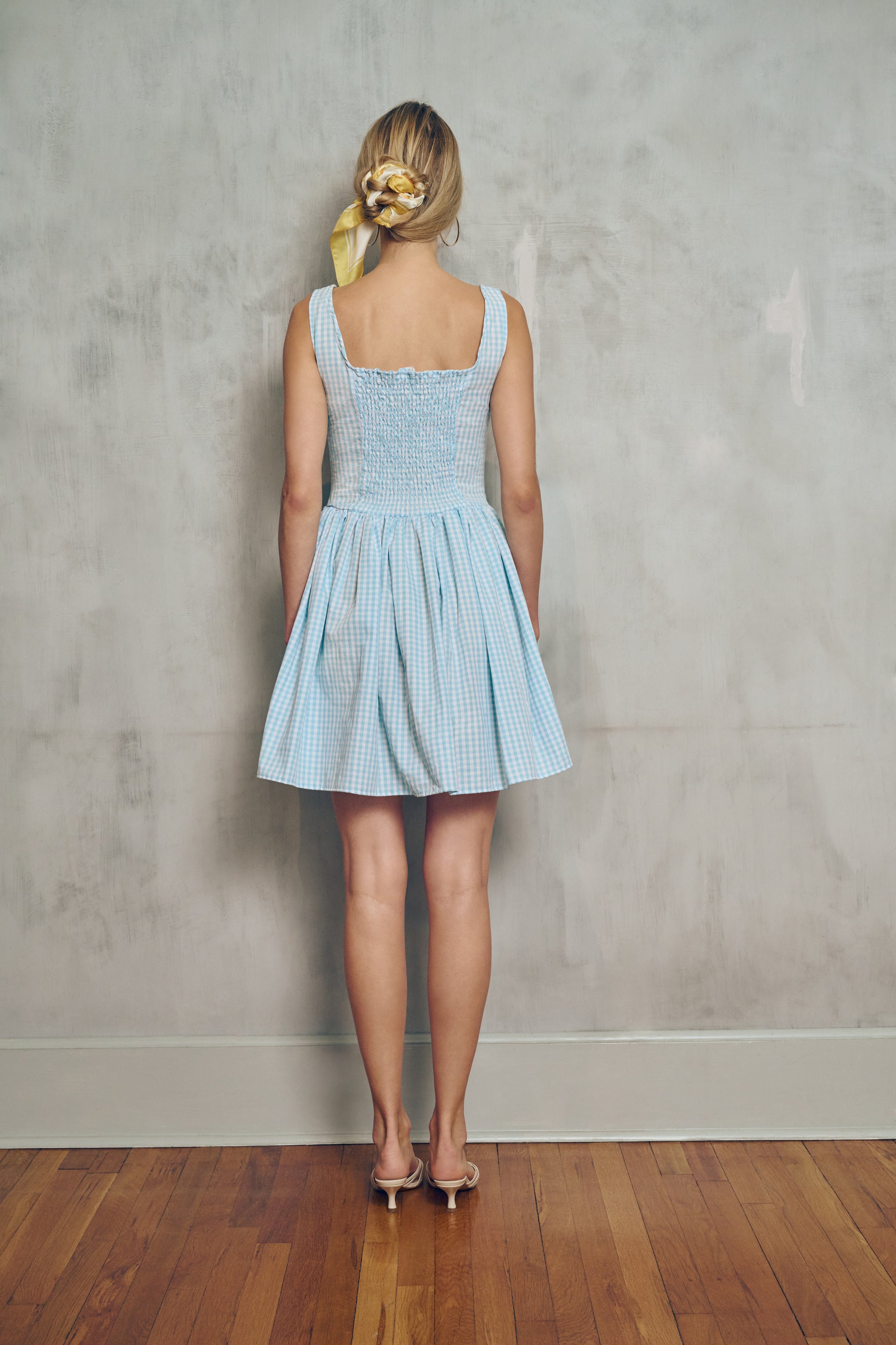 back view a Woman wearing a light blue checkered dress against a plain