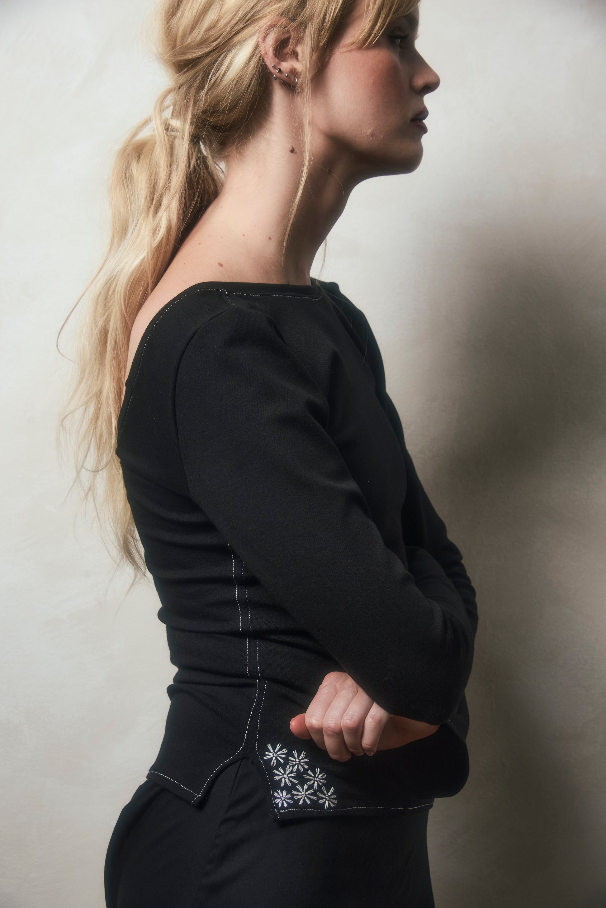 Woman wearing a black outfit with floral embroidery on a plain background
