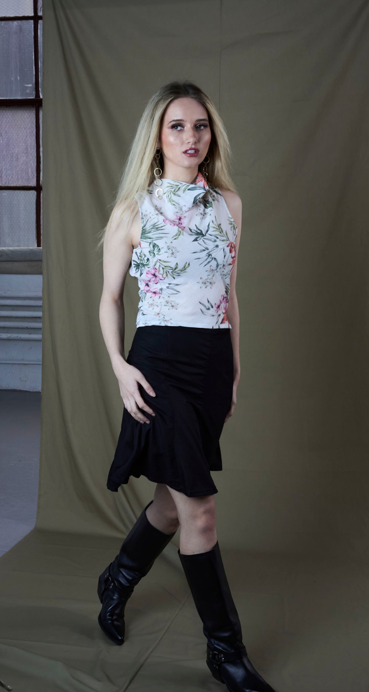 Woman wearing a floral top and black skirt with knee-high boots against a plain background