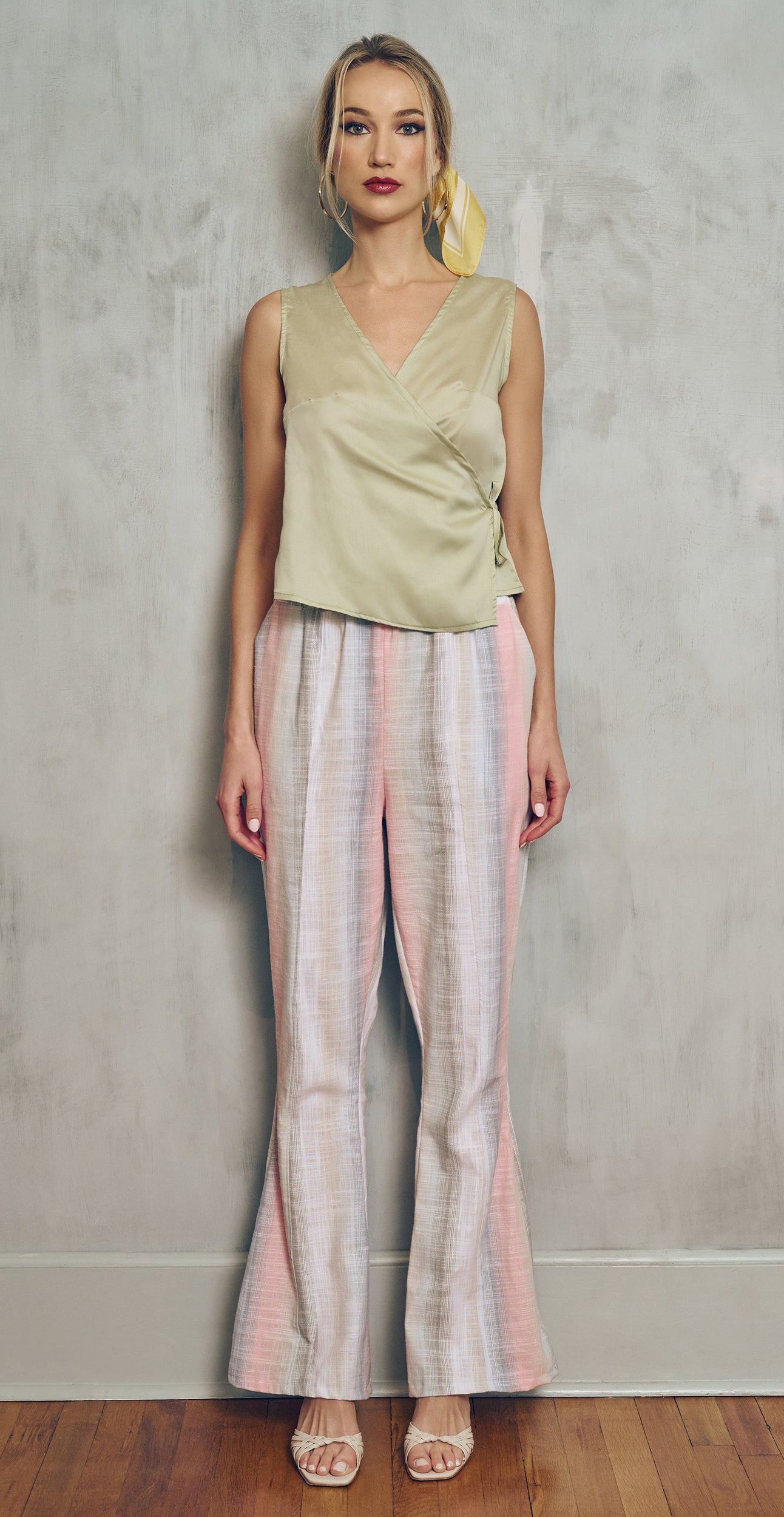 Woman wearing a light green sleeveless top and striped pants against a plain background