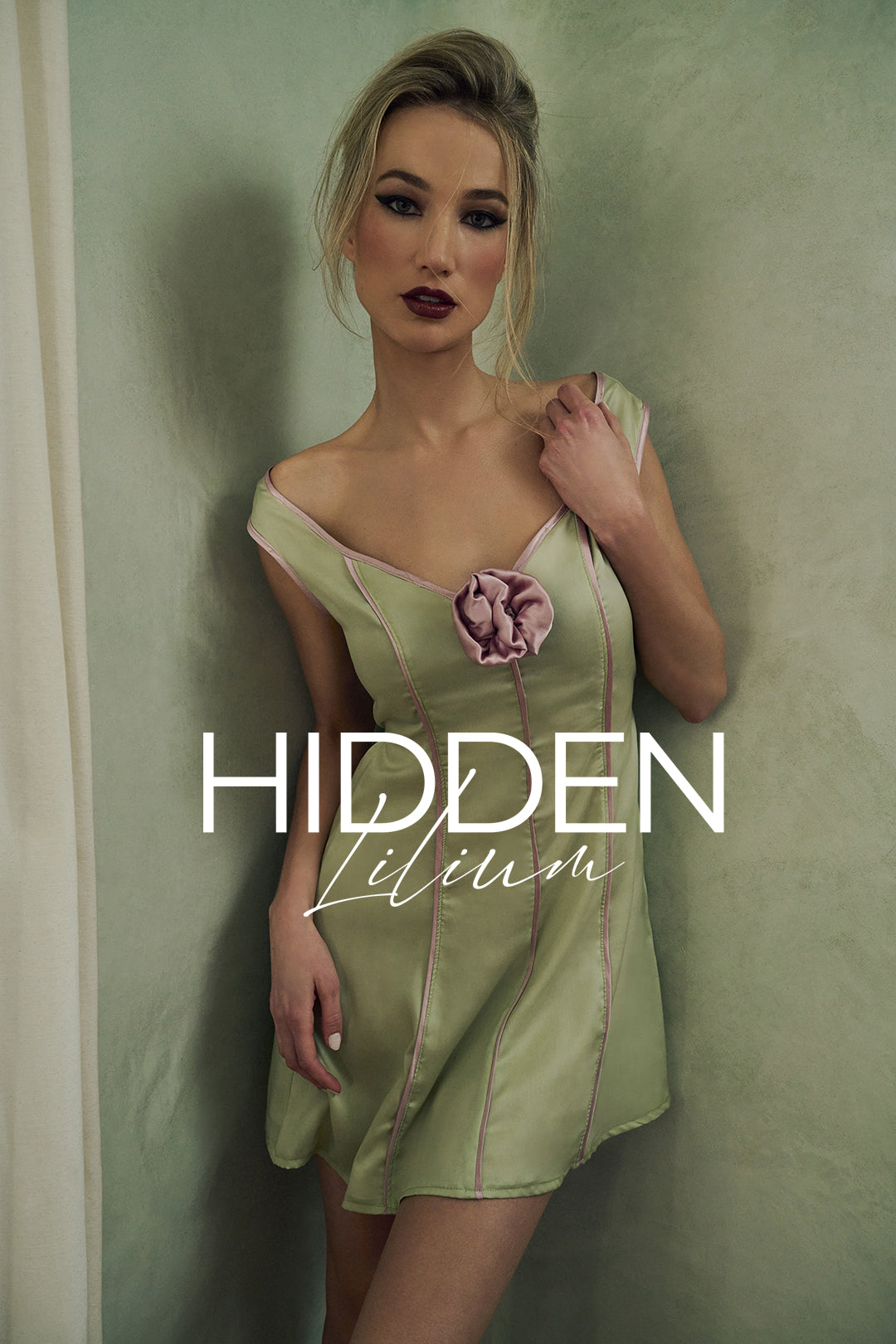 Woman wearing a green dress with a flower detail, standing against a plain wall with 'Hidden Lilium' branding.
