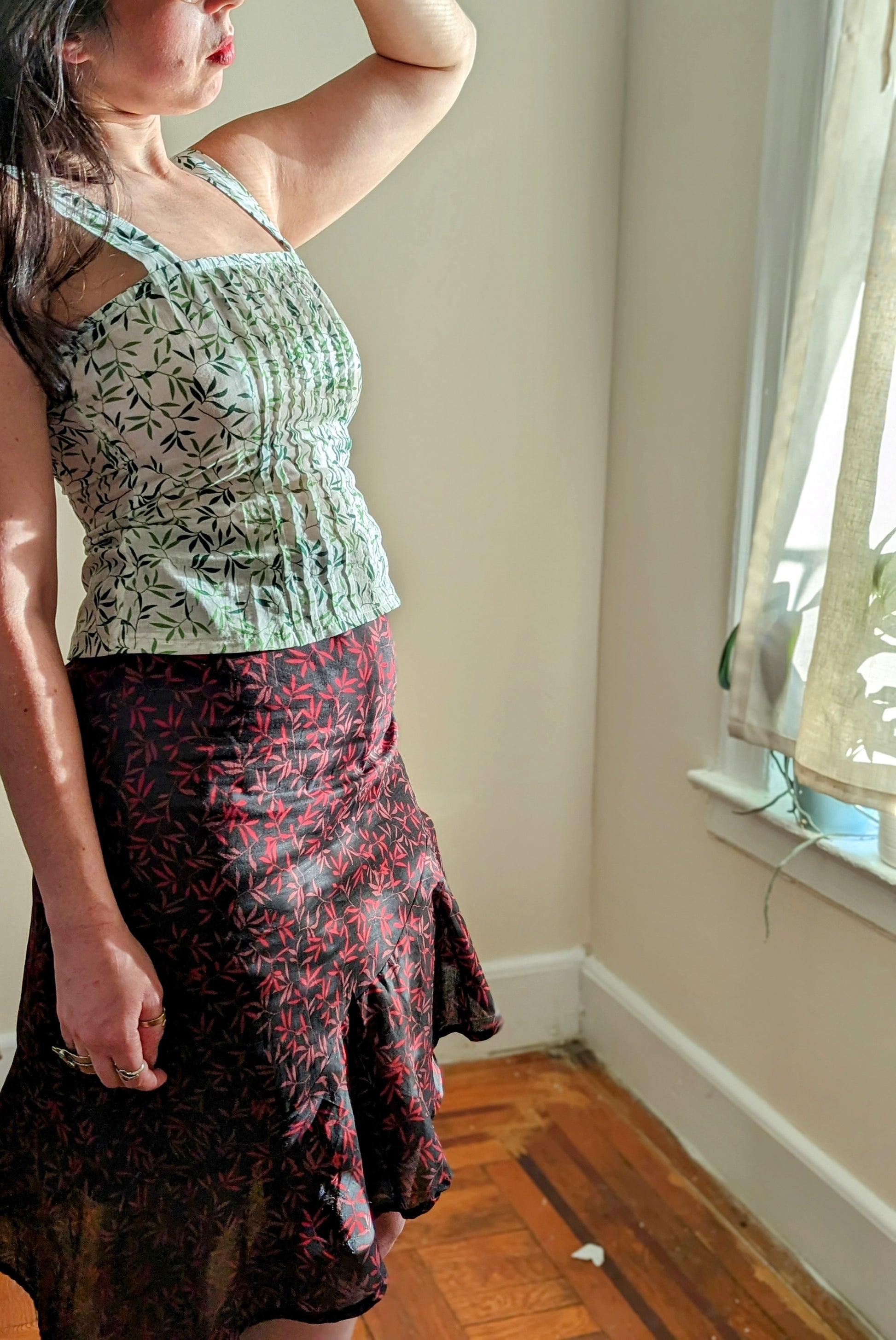 Woman wearing a green leaf patterned top and black floral skirt in a room with a window.