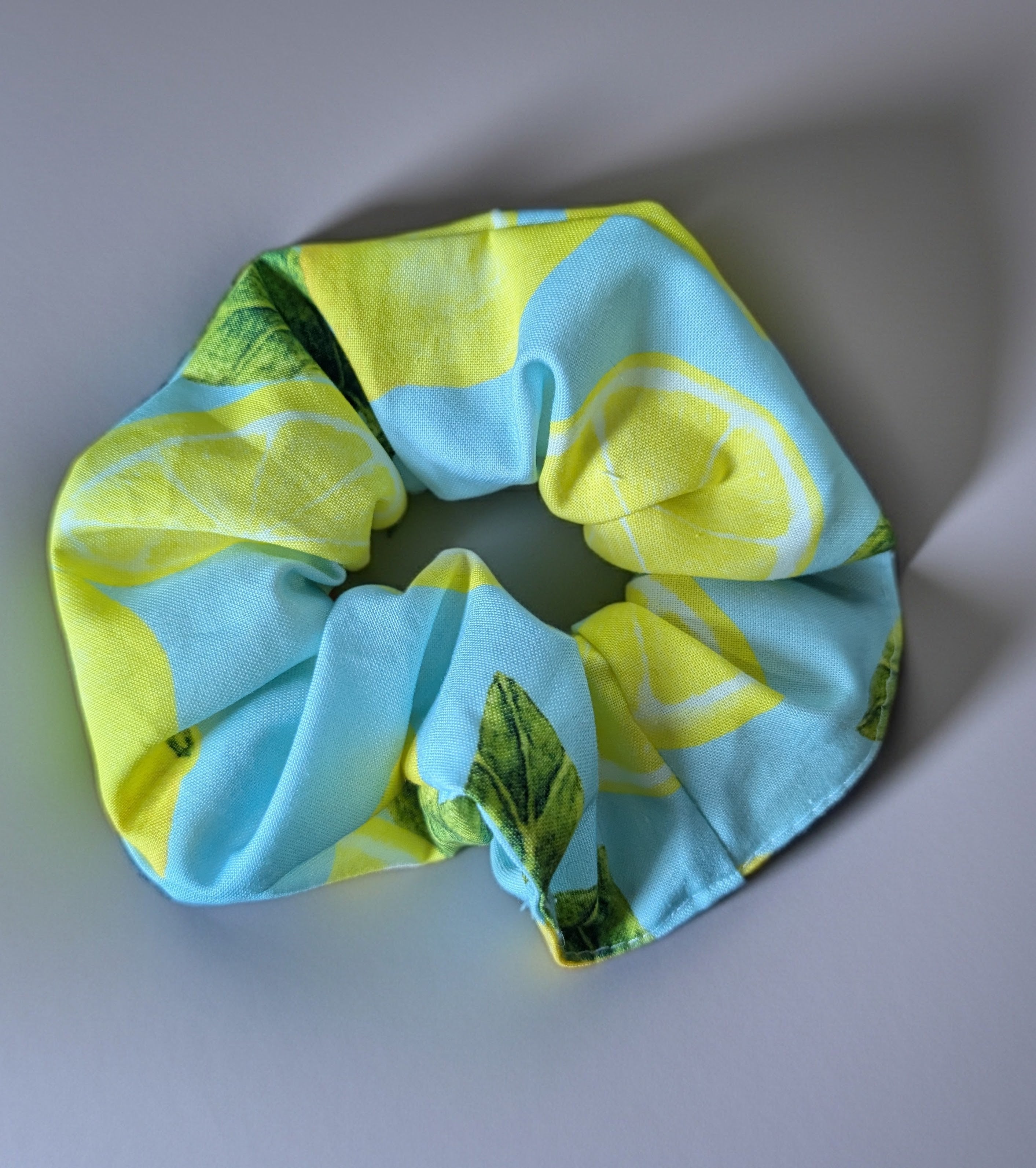Scrunchie with lemon and green leaf pattern on a light gray background