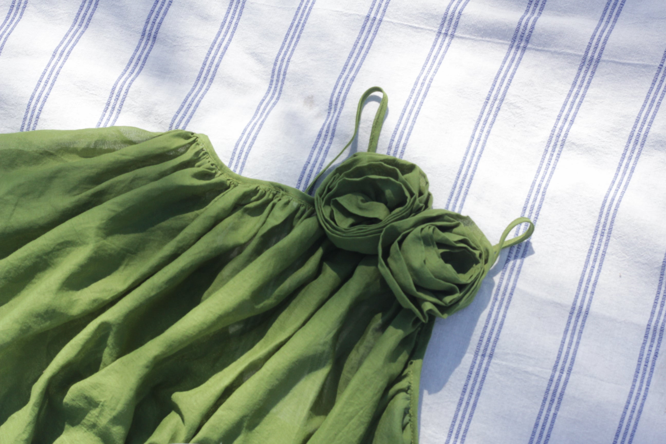 Green tank top with floral details on a white and blue striped fabric background